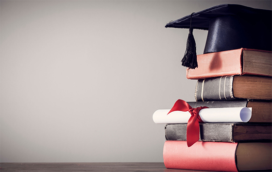 A grad cap and diploma sit on top of a stack of books